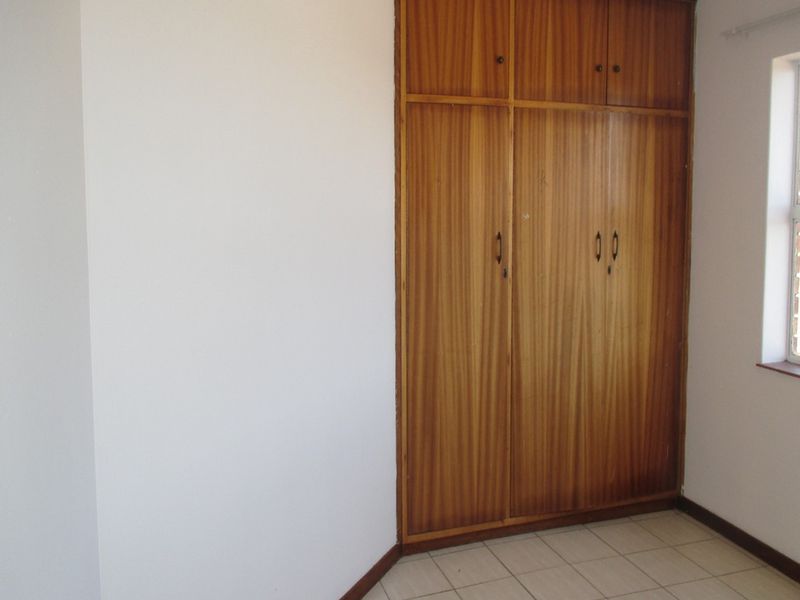 A vacant bedroom featuring built-in wooden wardrobes and tiled flooring, offering a clean and functional space ready for personalization.