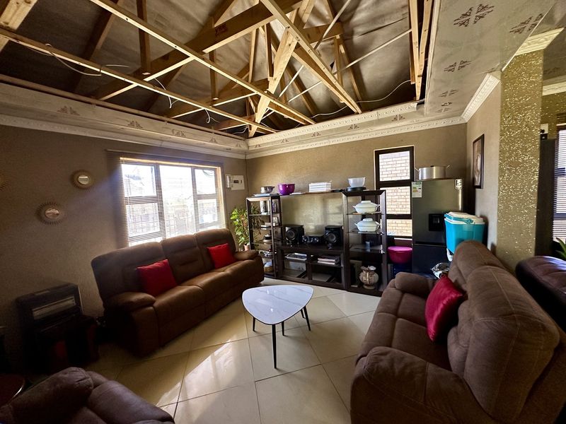 Living room featuring tiled flooring and decorative cornices, currently undergoing ceiling repairs with exposed roof trusses visible.