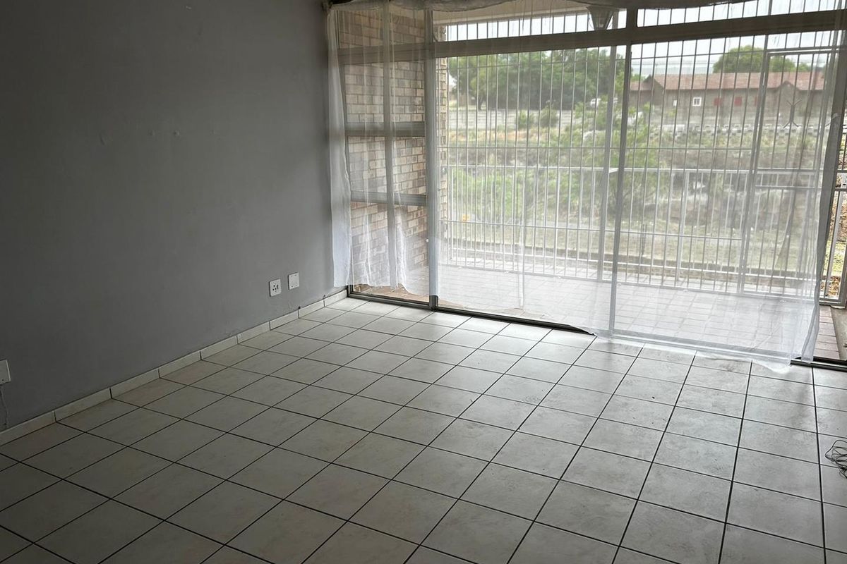 An empty living room featuring tiled flooring, large sliding glass doors with security bars, and access to an outdoor patio area.