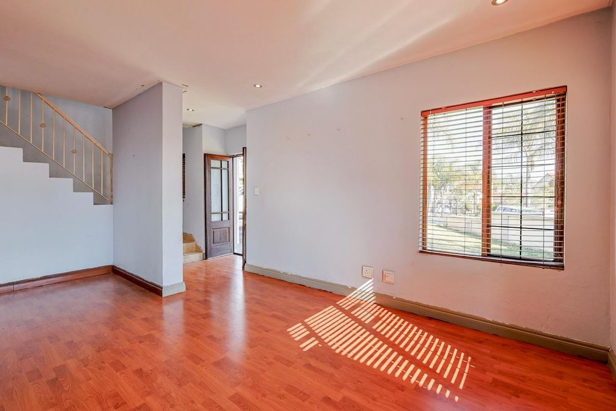 An empty living area featuring laminate flooring, a staircase with metal railing, and natural light through a window with venetian blinds.