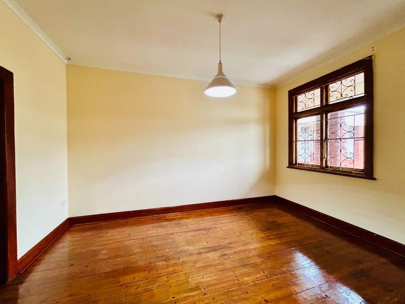 An empty bedroom featuring original timber flooring, timber-framed windows with security bars, and neutral wall finishes.