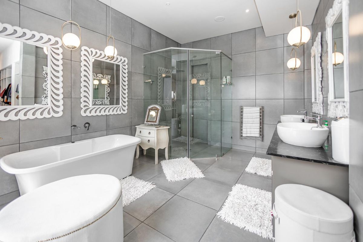 Modern bathroom featuring a freestanding bathtub, glass-enclosed corner shower, dual vessel sinks on a stone vanity, and large-format grey wall and floor tiles.