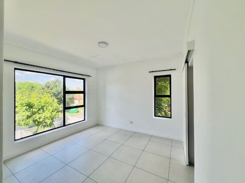 A bright, empty bedroom featuring large aluminium-framed windows, neutral tiled flooring, and a sliding door, offering a clean and modern blank canvas.