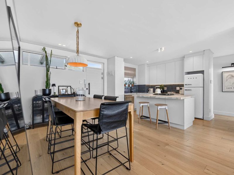 Modern open-plan kitchen and dining area featuring light timber flooring, sleek white cabinetry, a stone-topped island, and contemporary recessed lighting.