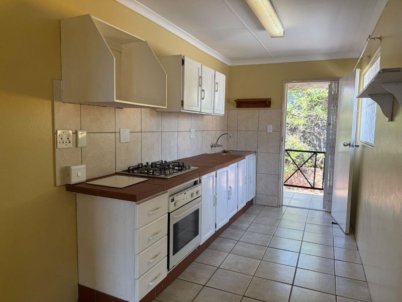 A functional kitchen featuring built-in cabinetry, a gas hob, an oven, and tiled finishes, with direct access to an outdoor area.