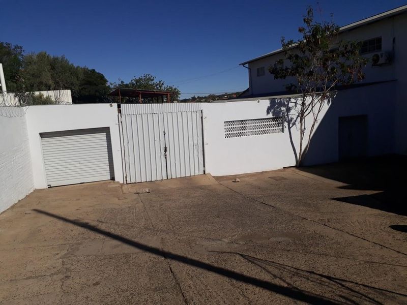 Rear exterior view of the industrial property featuring a concrete yard, secure metal gate, and a roller shutter door access point.