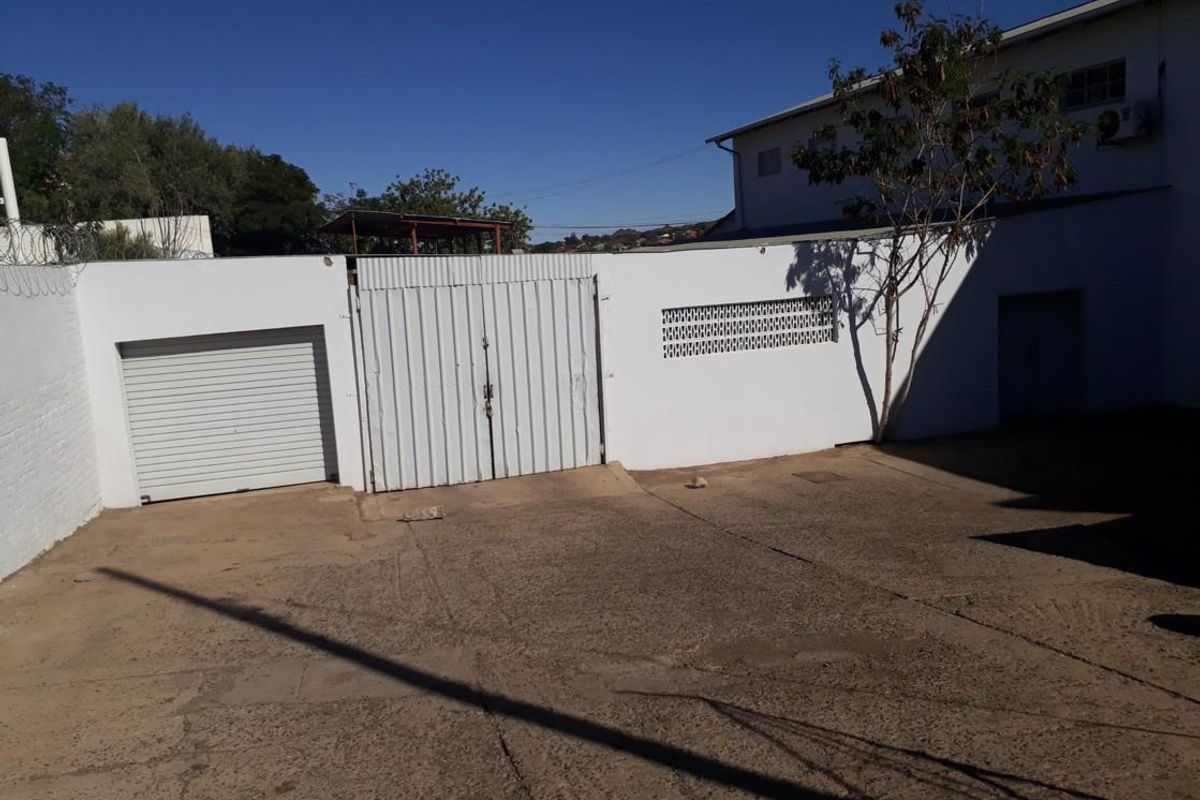 Rear exterior view of the industrial property featuring a concrete yard, secure metal gate, and a roller shutter door access point.