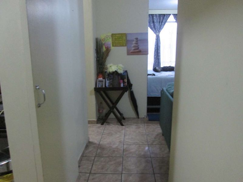 A tiled hallway area providing access to adjacent living spaces, featuring neutral wall finishes and a built-in storage cupboard.