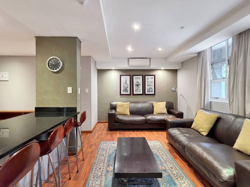 Spacious open-plan living area featuring a granite breakfast bar, modern recessed lighting, split-system air conditioning, and warm laminate flooring.