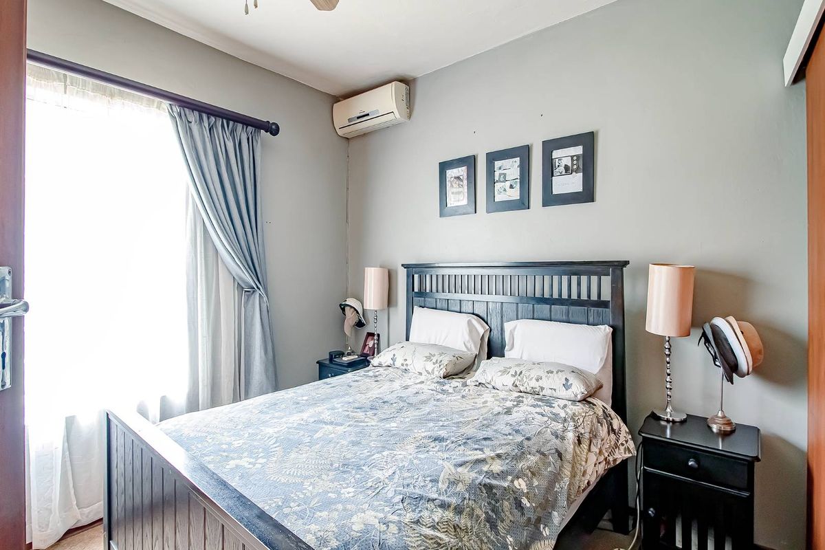 A cozy bedroom featuring a wall-mounted air conditioning unit, large window with curtain rod, and neutral wall finishes.