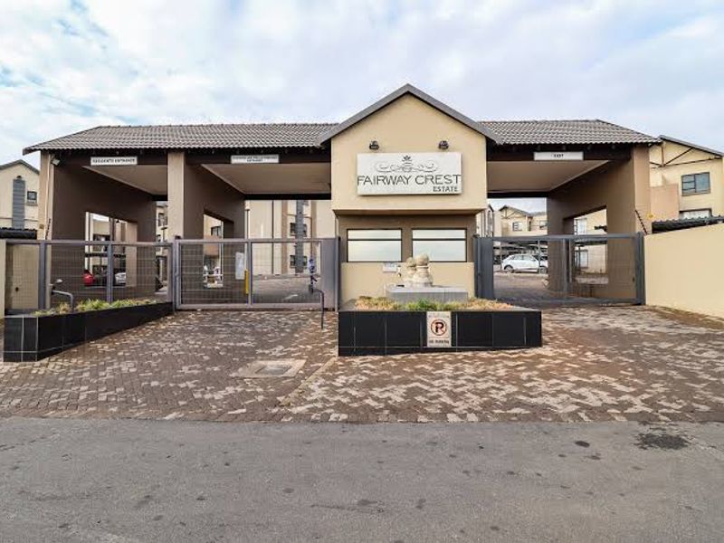 Main entrance gate and security access point for Fairway Crest Estate, featuring paved driveway and secure perimeter fencing.