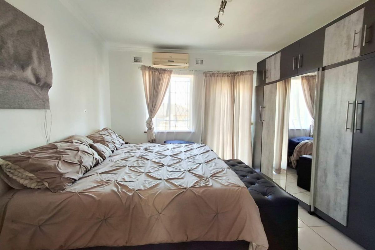 Spacious bedroom featuring tiled flooring, built-in cupboards with mirrored doors, and a wall-mounted air conditioning unit.