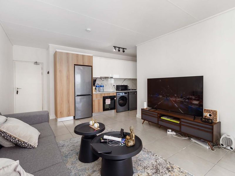Modern open-plan living area featuring a compact kitchen with built-in cabinetry, integrated oven, and tiled flooring throughout.