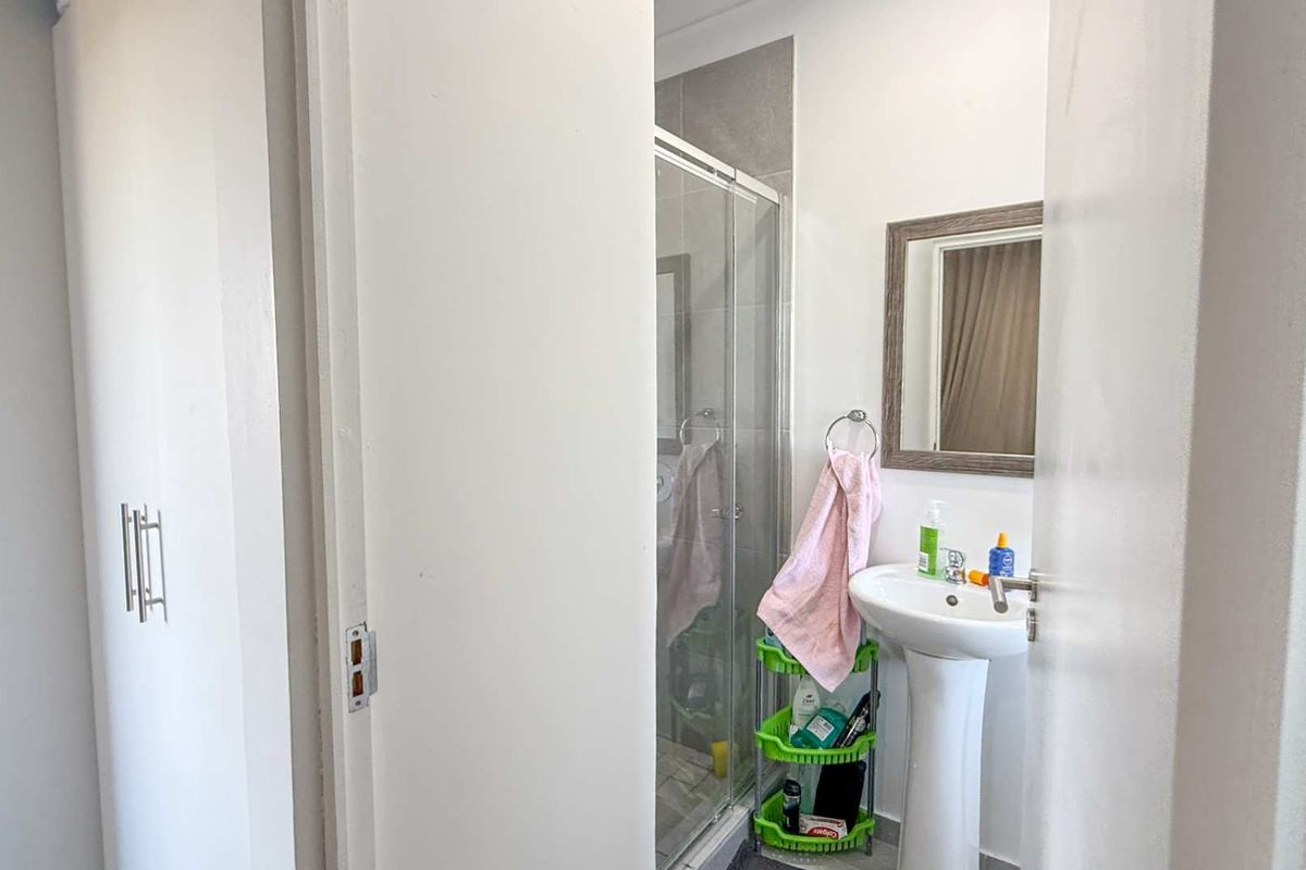 A compact bathroom featuring a pedestal sink, a framed mirror, and a glass-enclosed shower stall with tiled walls.