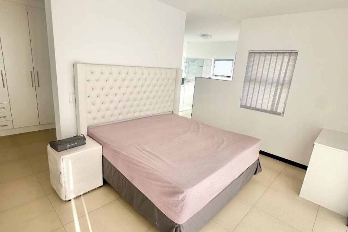 A bright bedroom featuring neutral floor tiles, built-in wardrobes, and a semi-open layout with an adjacent bathroom area.