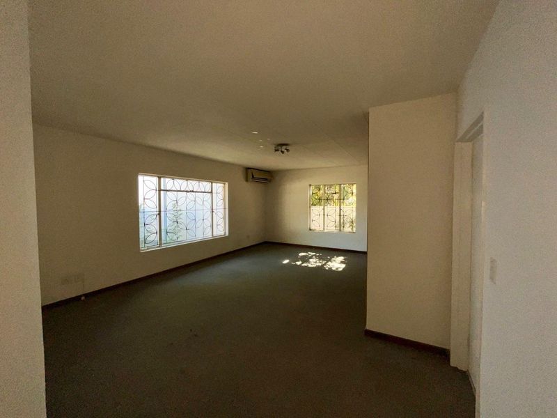 A spacious, empty living area featuring carpet flooring, split-system air conditioning, and security bars on the windows.