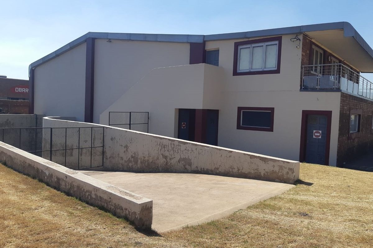 Rear exterior view of the retail property featuring a concrete access ramp, external staircase, and upper-level balcony with glass balustrades.