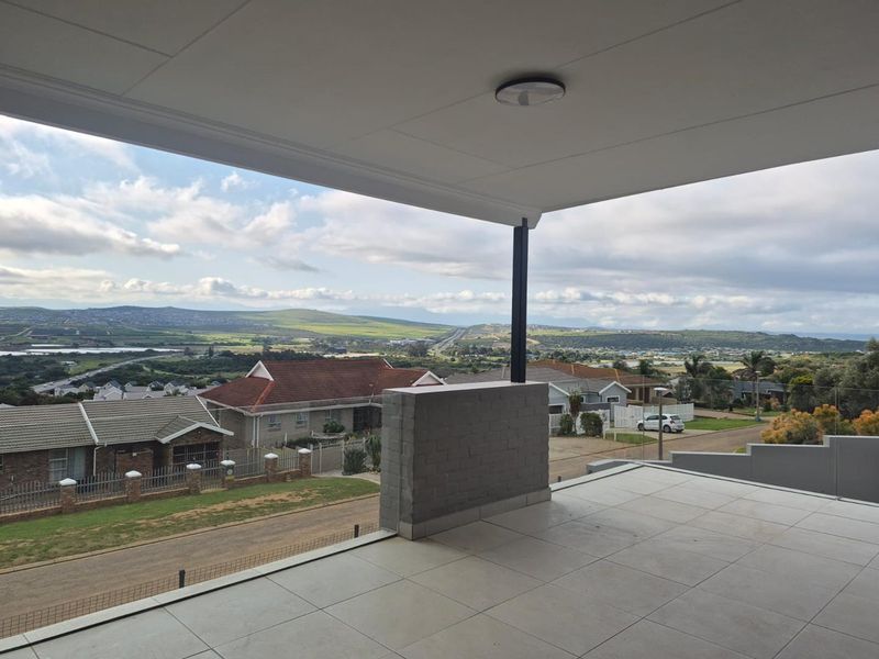 A spacious covered balcony featuring tiled flooring and a brick balustrade, offering expansive elevated views of the surrounding neighbourhood and landscape.