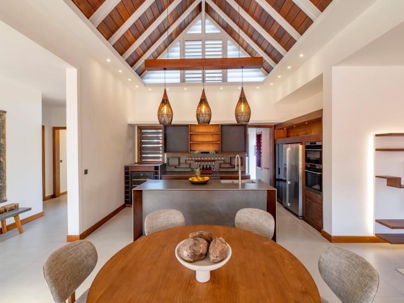 A modern open-plan kitchen featuring a central island, high-end built-in appliances, and a striking vaulted timber-paneled ceiling with recessed lighting.