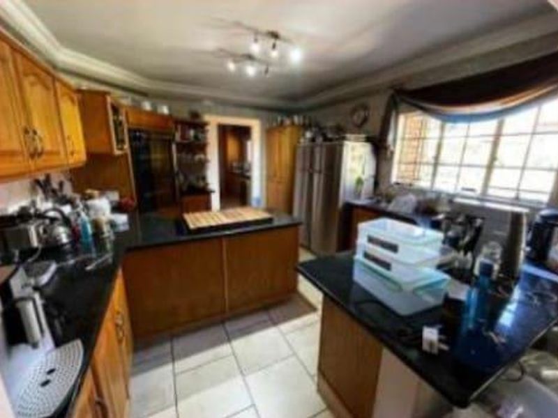 A spacious kitchen featuring wooden cabinetry, granite countertops, a central island, and tiled flooring, offering ample workspace and storage.