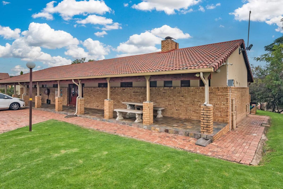 A view of the exterior rear of the townhouse, featuring a covered patio area with brick pillars, tiled flooring, and a terracotta roof.