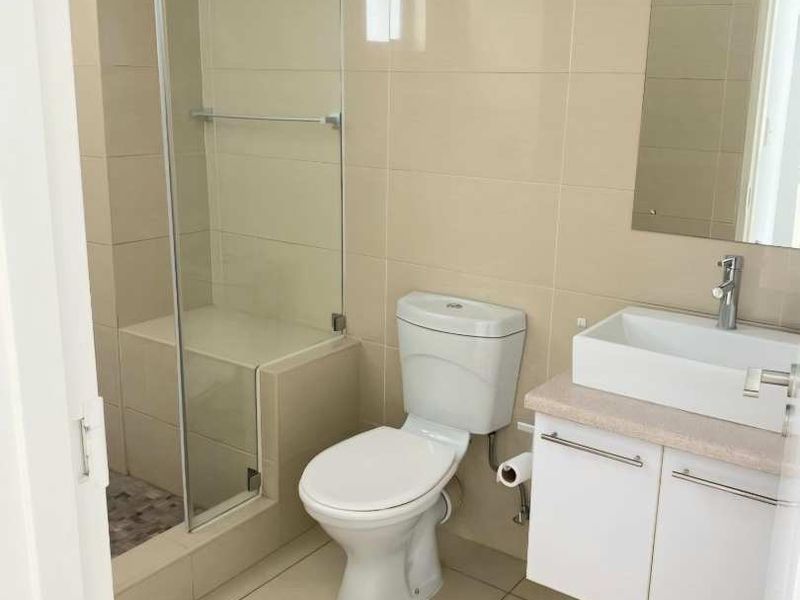 Modern bathroom featuring a glass-enclosed shower with a built-in bench, wall-mounted vanity with basin, and neutral floor-to-ceiling tiling.