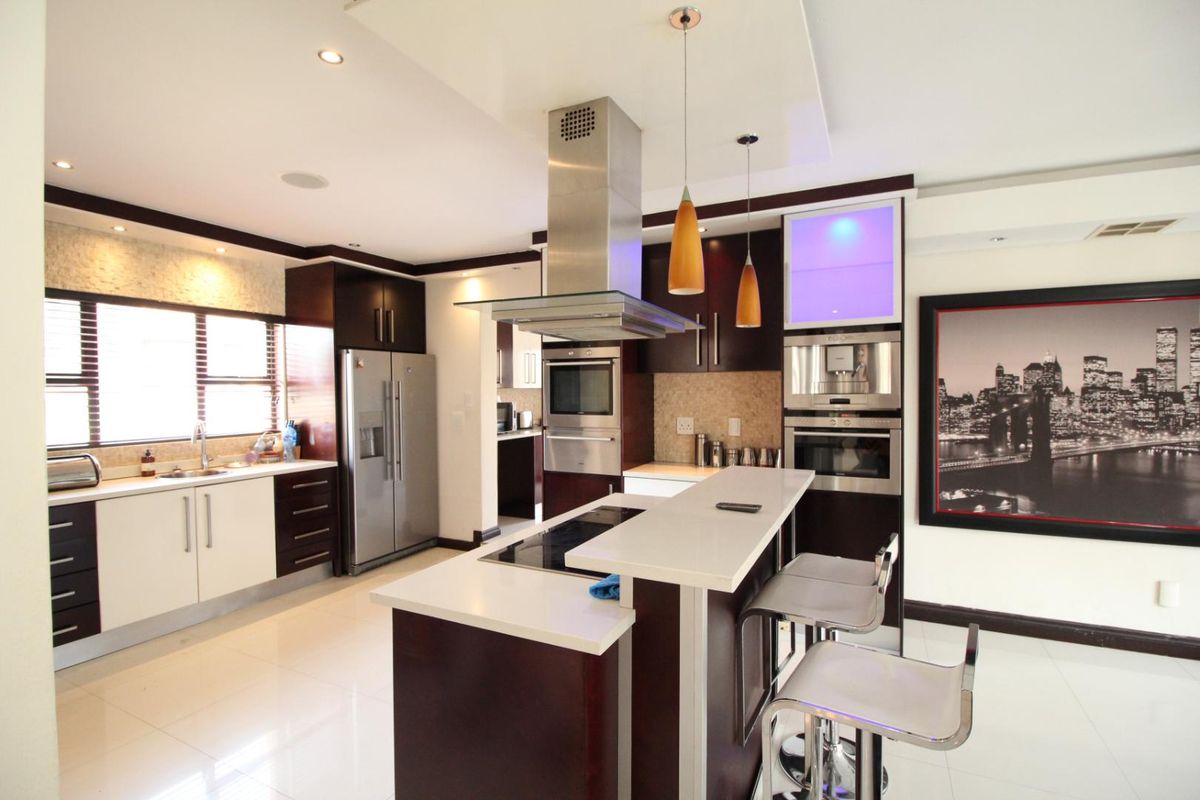 Modern kitchen featuring a central island with breakfast bar, built-in stainless steel appliances, dark cabinetry, and contrasting white countertops.