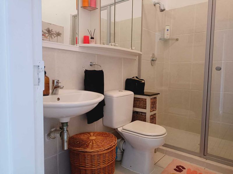 A functional bathroom featuring a pedestal basin, toilet, and a glass-enclosed shower with neutral wall and floor tiling.