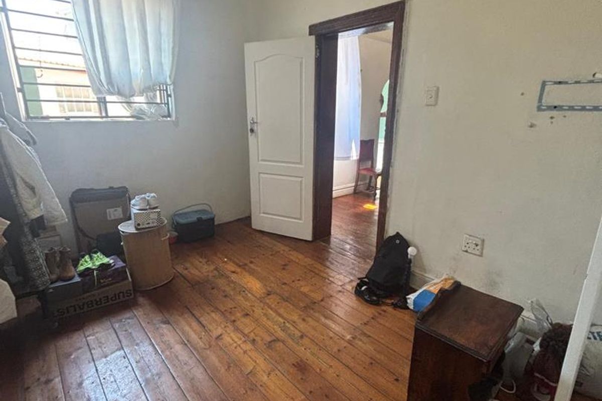 A bedroom featuring original timber flooring, a window with security bars, and a doorway leading to an adjacent room.