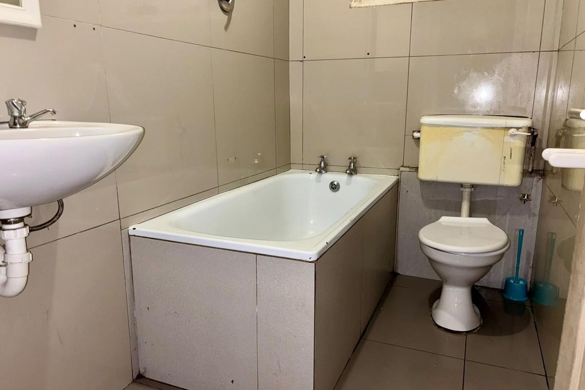A functional bathroom featuring a bathtub, wall-mounted basin, and toilet with full-height wall tiling, requiring cosmetic updates to modernize the space.