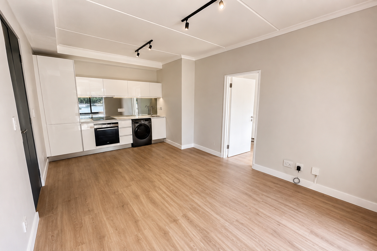 Modern open-plan living area featuring a sleek, white kitchen with integrated appliances, track lighting, and light wood-look laminate flooring throughout.