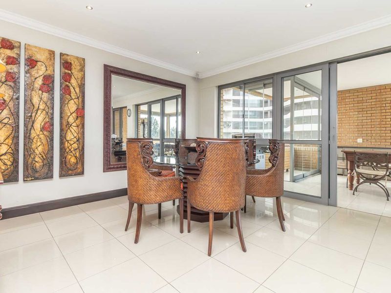 A bright dining room featuring large porcelain floor tiles, recessed downlighting, and sliding glass doors that open onto a covered balcony area.