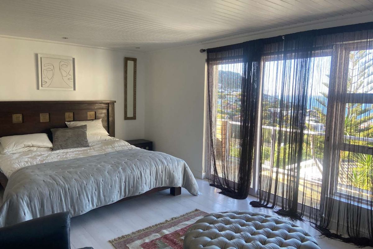 Spacious bedroom featuring timber-paneled ceilings, light-toned flooring, and large sliding glass doors opening to a balcony with scenic coastal views.