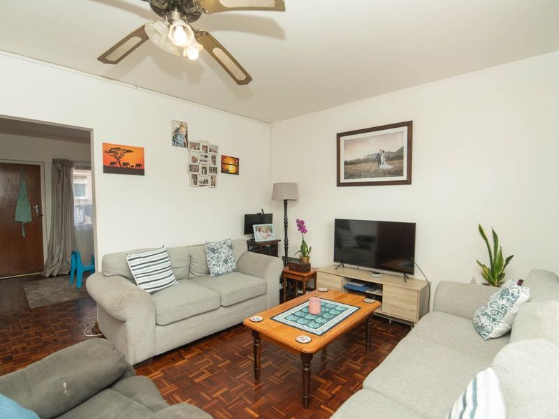 A comfortable living room featuring classic parquet flooring and a ceiling fan, providing a functional and inviting space for relaxation.