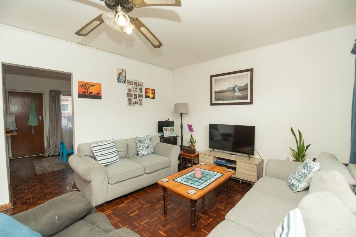 A comfortable living room featuring classic parquet flooring and a ceiling fan, providing a functional and inviting space for relaxation.