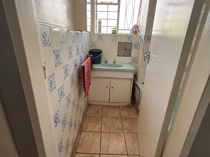 A compact bathroom featuring dated blue and white patterned wall tiles, a vanity cabinet with a basin, and tiled flooring.
