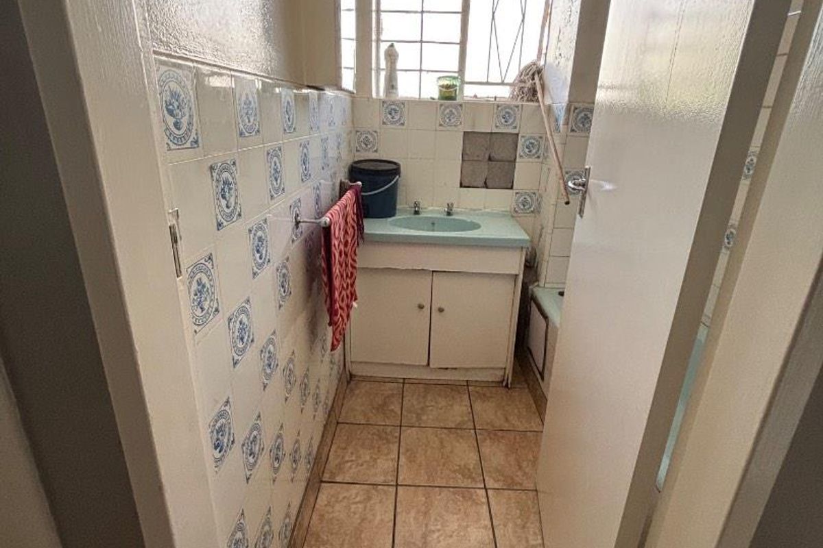A compact bathroom featuring dated blue and white patterned wall tiles, a vanity cabinet with a basin, and tiled flooring.