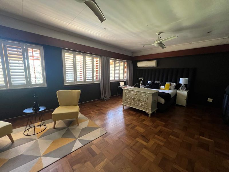 Spacious bedroom featuring rich parquet flooring, plantation shutters, a ceiling fan, and a wall-mounted air conditioning unit.