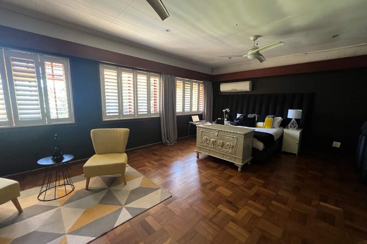 Spacious bedroom featuring rich parquet flooring, plantation shutters, a ceiling fan, and a wall-mounted air conditioning unit.