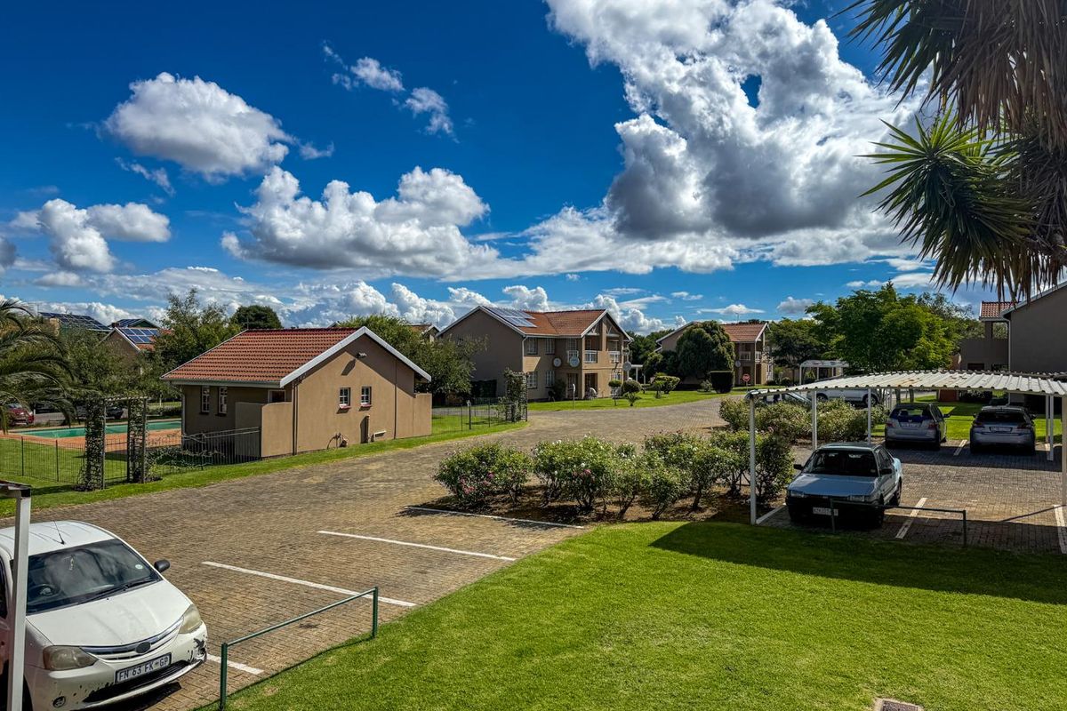 An elevated view of the apartment complex grounds featuring paved parking areas, carports, and well-maintained communal lawns under a clear blue sky.