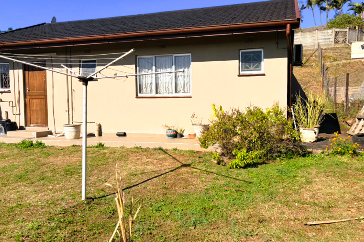 Rear view of the townhouse featuring a paved patio area, tiled roof, and a private garden space with a rotary clothesline.