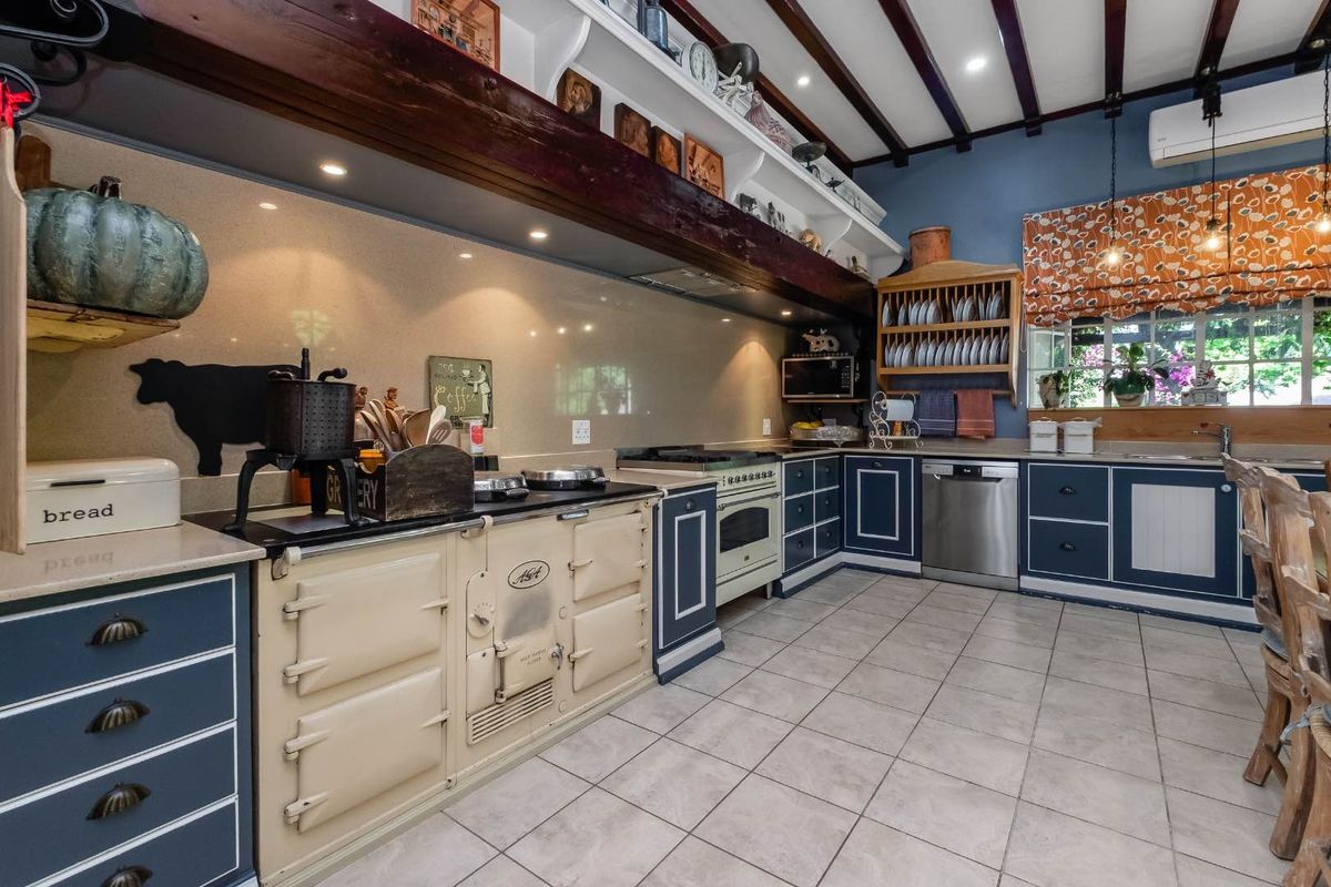 A characterful kitchen featuring a classic Aga range cooker, exposed timber ceiling beams, tiled flooring, and ample built-in cabinetry with a solid surface splashback.
