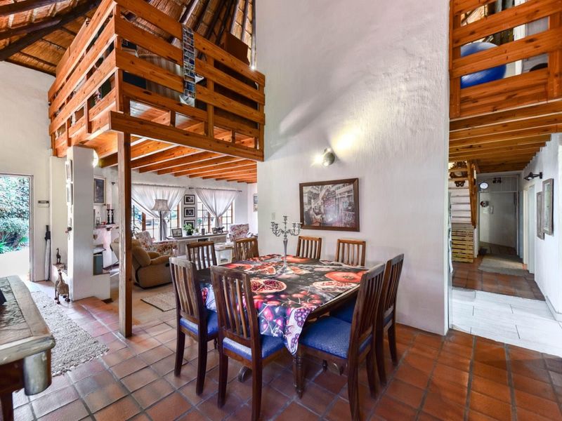 Open-plan living and dining area featuring terracotta flooring, a high thatched ceiling with exposed timber beams, and a mezzanine loft level.