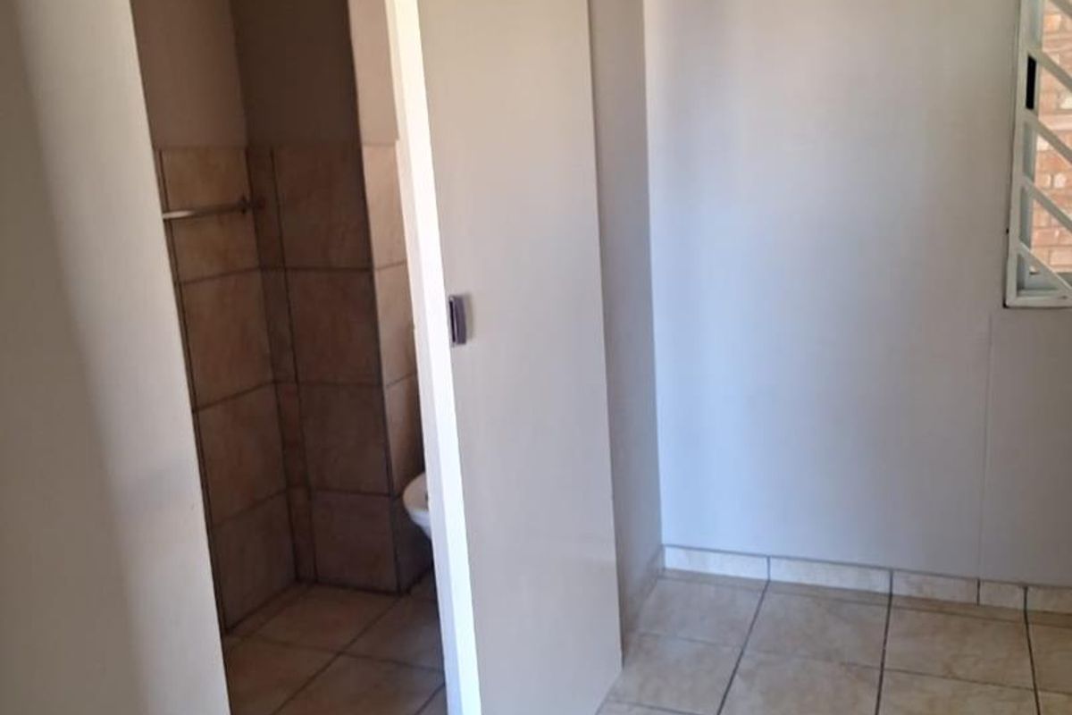 A functional bathroom space featuring tiled flooring, a sliding door entry, and a window with security bars.