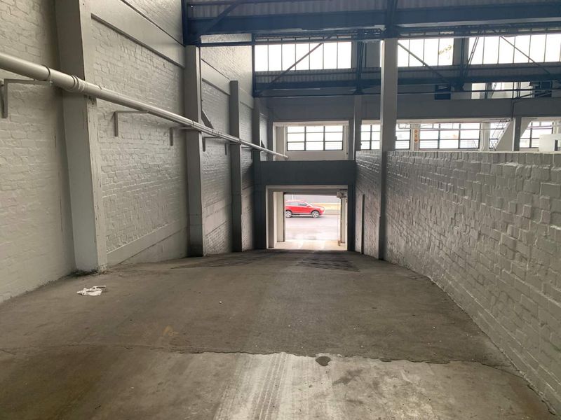 Industrial garage space featuring a concrete ramp, painted brick walls, and exposed steel structural elements with high-level industrial windows.