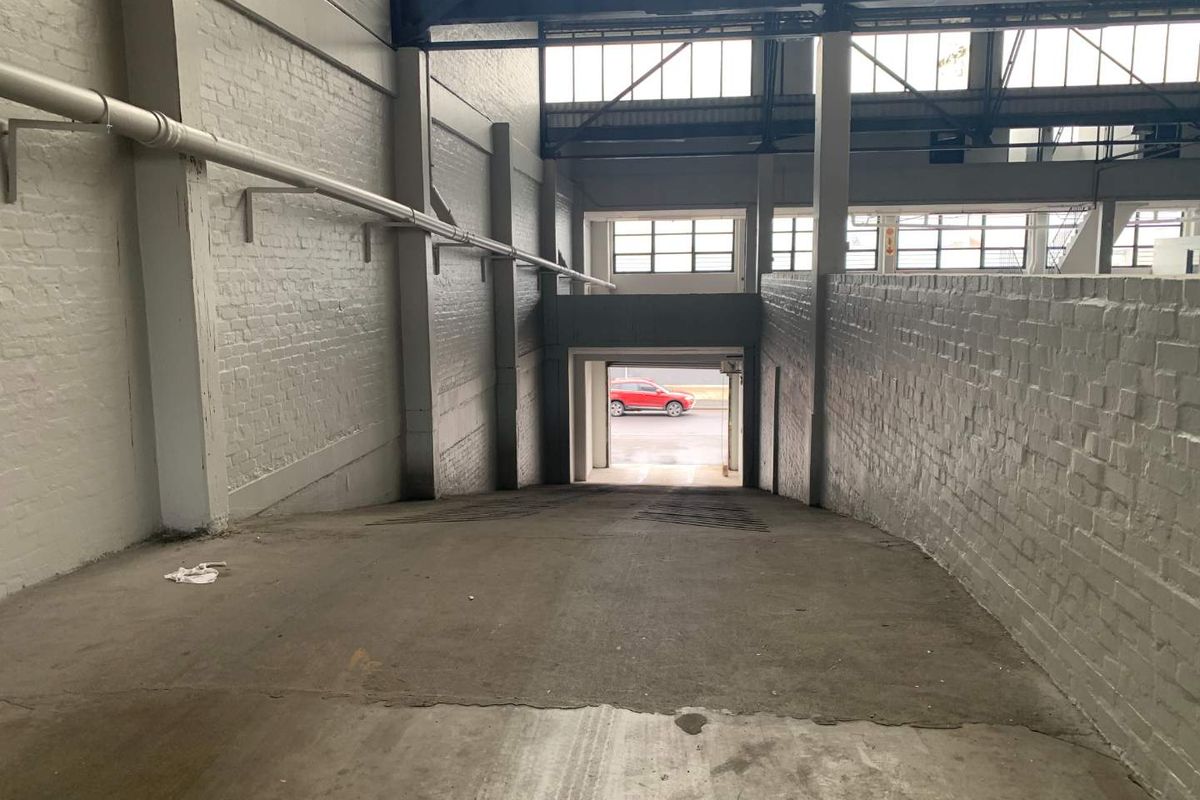 Industrial garage space featuring a concrete ramp, painted brick walls, and exposed steel structural elements with high-level industrial windows.