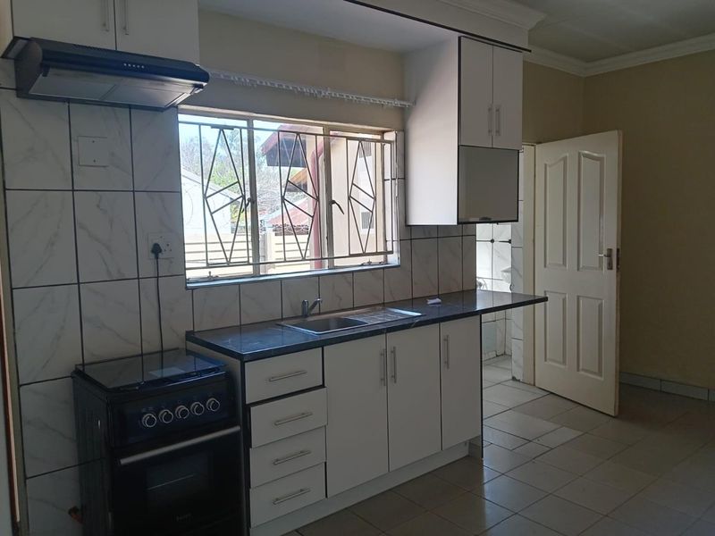 A functional kitchen featuring white cabinetry, a stainless steel sink, tiled backsplash, and an extractor fan, with direct access to an adjacent room.