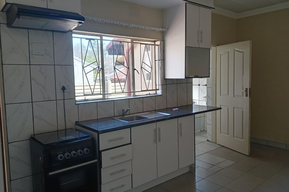 A functional kitchen featuring white cabinetry, a stainless steel sink, tiled backsplash, and an extractor fan, with direct access to an adjacent room.