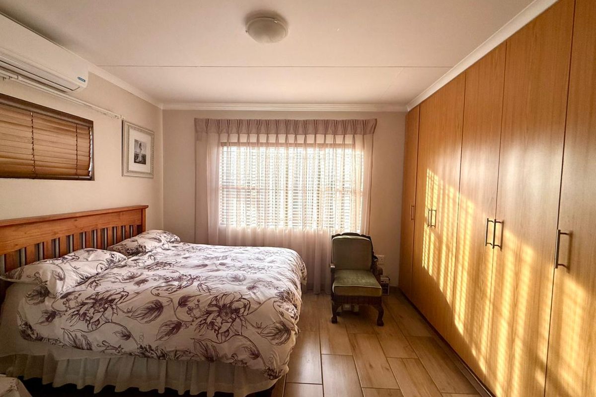 A well-lit bedroom featuring wood-look tile flooring, extensive built-in wooden cabinetry, and a wall-mounted air conditioning unit.