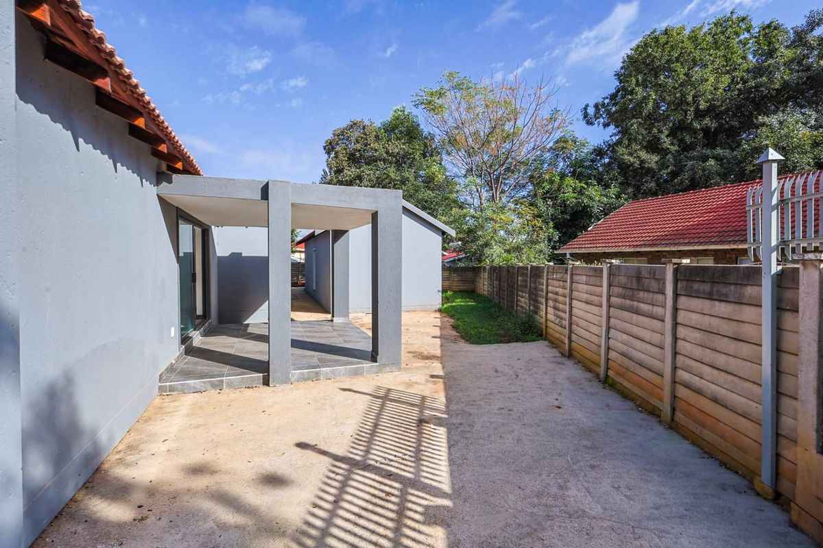 Rear exterior view featuring a covered patio with tiled flooring, adjacent to a side yard with a precast concrete boundary wall.